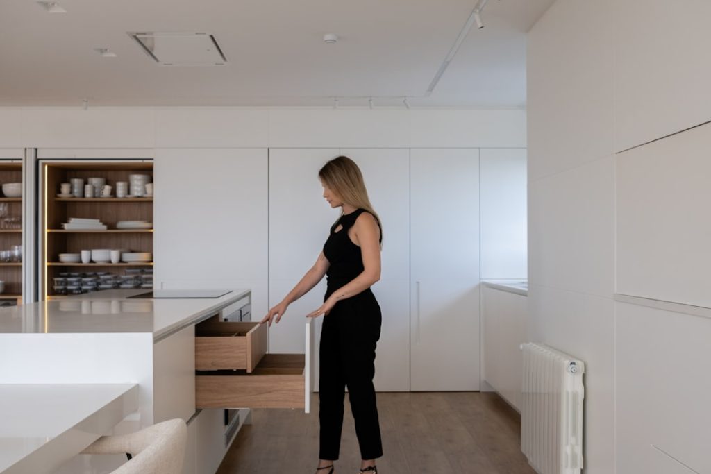 Woman opening kitchen cabinet drawer with organized items inside.